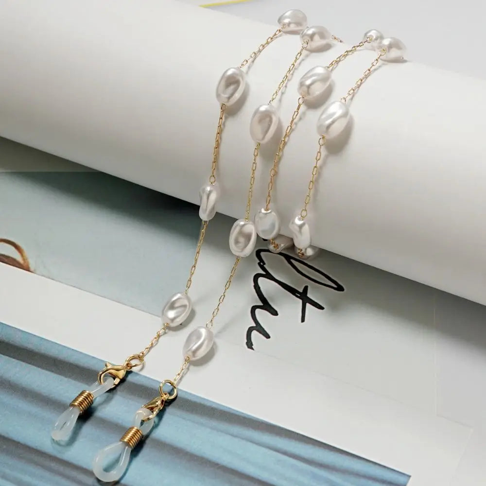 Collares para gafas de perlas y cuentas tono dorado exhibidos sobre un fondo claro.