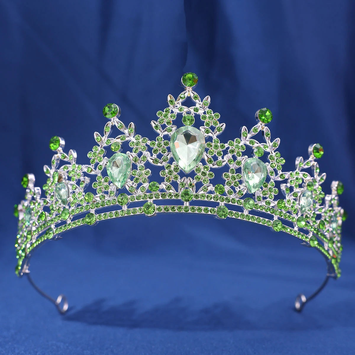 An elegant crystal rhinestone tiara and headband set with green gemstones against a blue background.