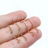 A hand holds several gold-finished stainless steel nostril studs with crystal accents.
