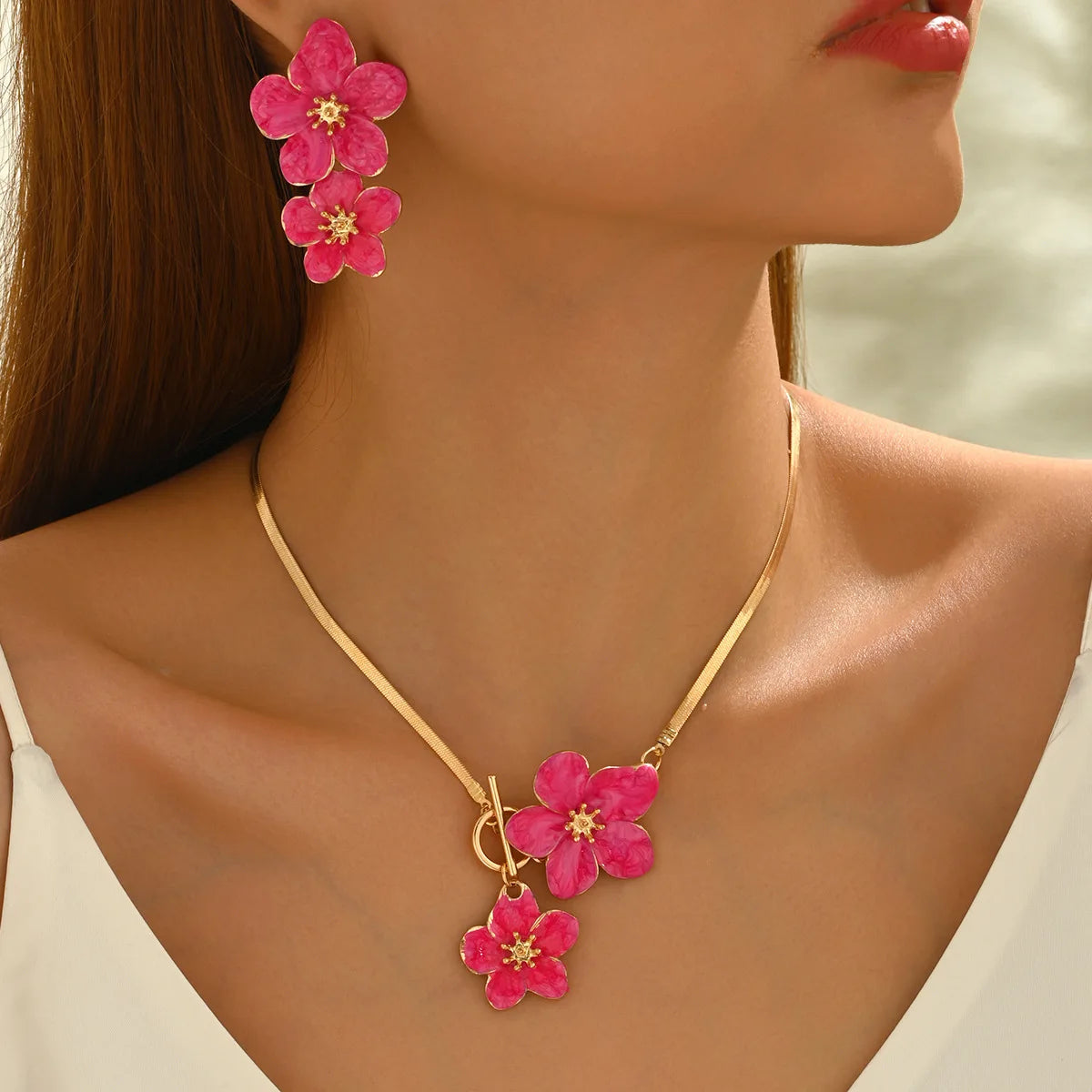 A close-up of a woman wearing a gold floral pendant necklace and matching earrings with pink flowers.