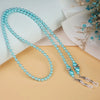 Two strands of light blue pearl beaded chains laid on a beige surface with a white background and dried floral elements.