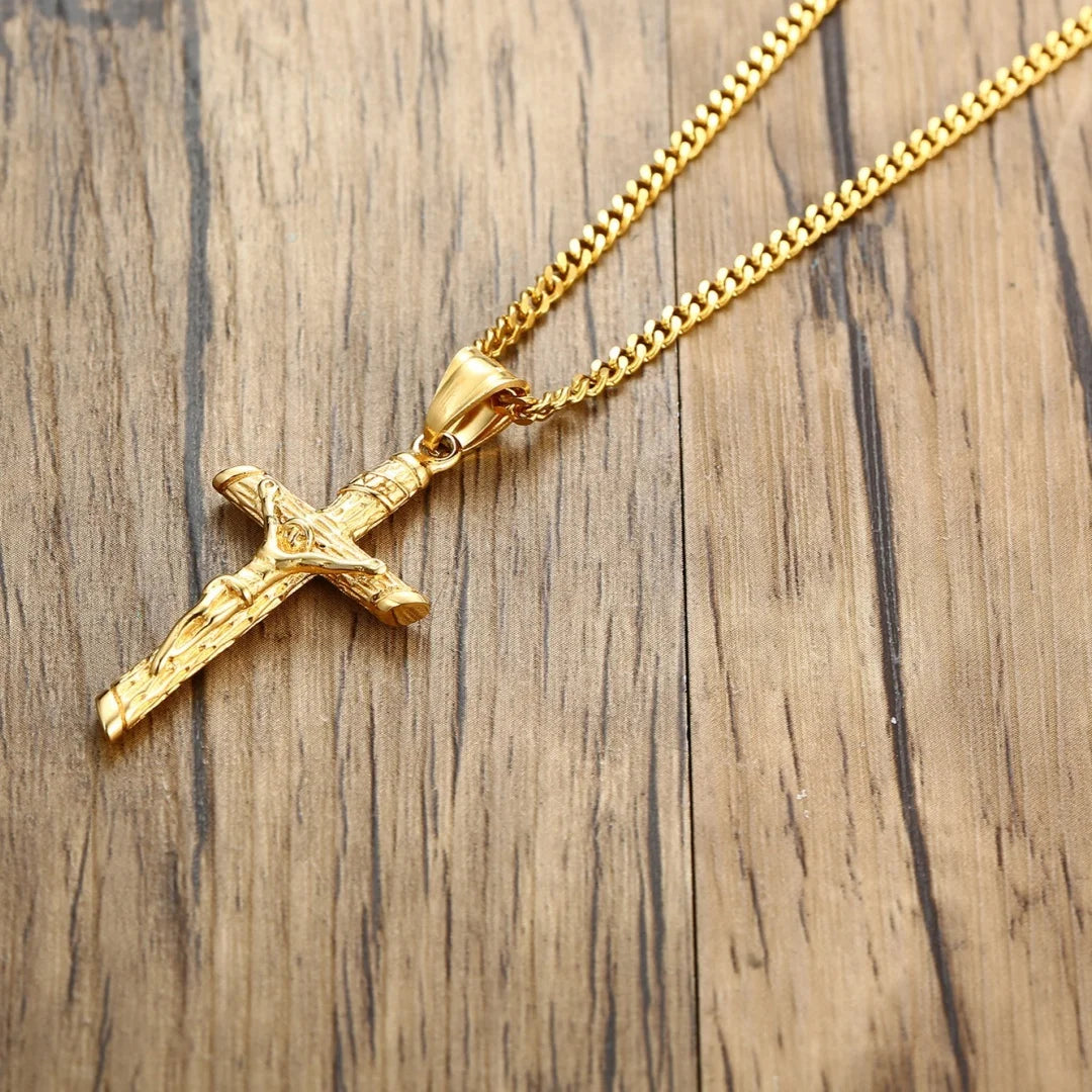 A gold-finished stainless steel cross necklace with a chain resting on a wooden surface.