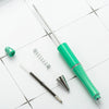 A green beadable ballpoint pen and a metal spring are shown on a white surface.