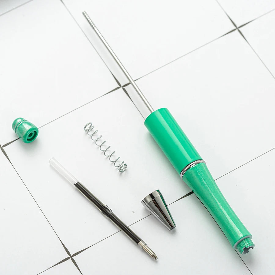 A green beadable ballpoint pen and a metal spring are shown on a white surface.