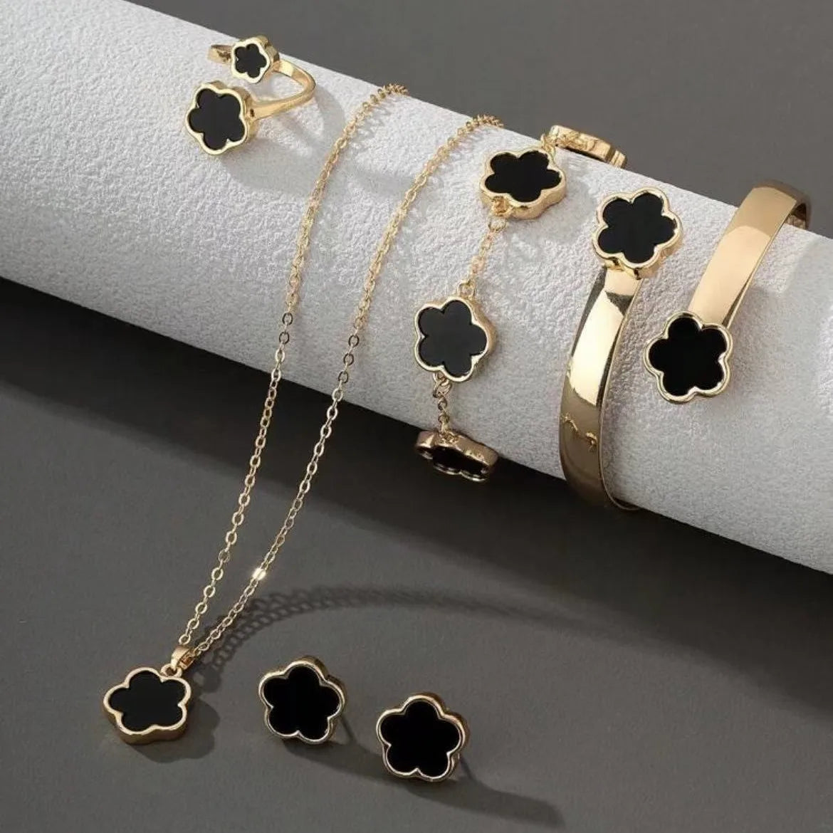 A set of five gold-toned bracelets featuring black enamel plum blossom charms displayed on a white surface.
