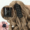 A close-up view of a black claw clip ponytail extension being installed in long, wavy blonde hair.