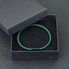 A green thread charm bracelet is displayed inside a black box with a lid, set against a dark gray background.