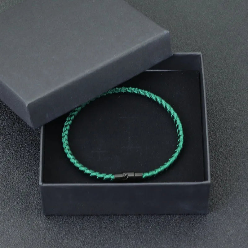 A green thread charm bracelet is displayed inside a black box with a lid, set against a dark gray background.