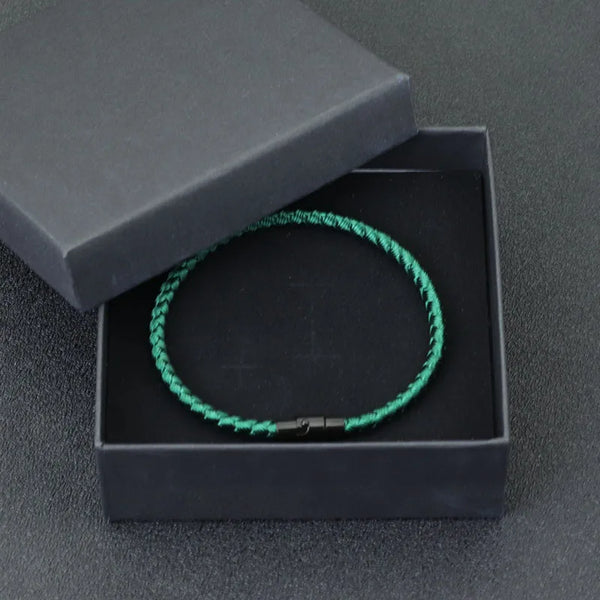 A green thread charm bracelet is displayed inside a black box with a lid, set against a dark gray background.