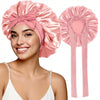 Una mujer modela un gorro de dormir de satén rosa con un gran lazo y cintas para el cabello a juego.
