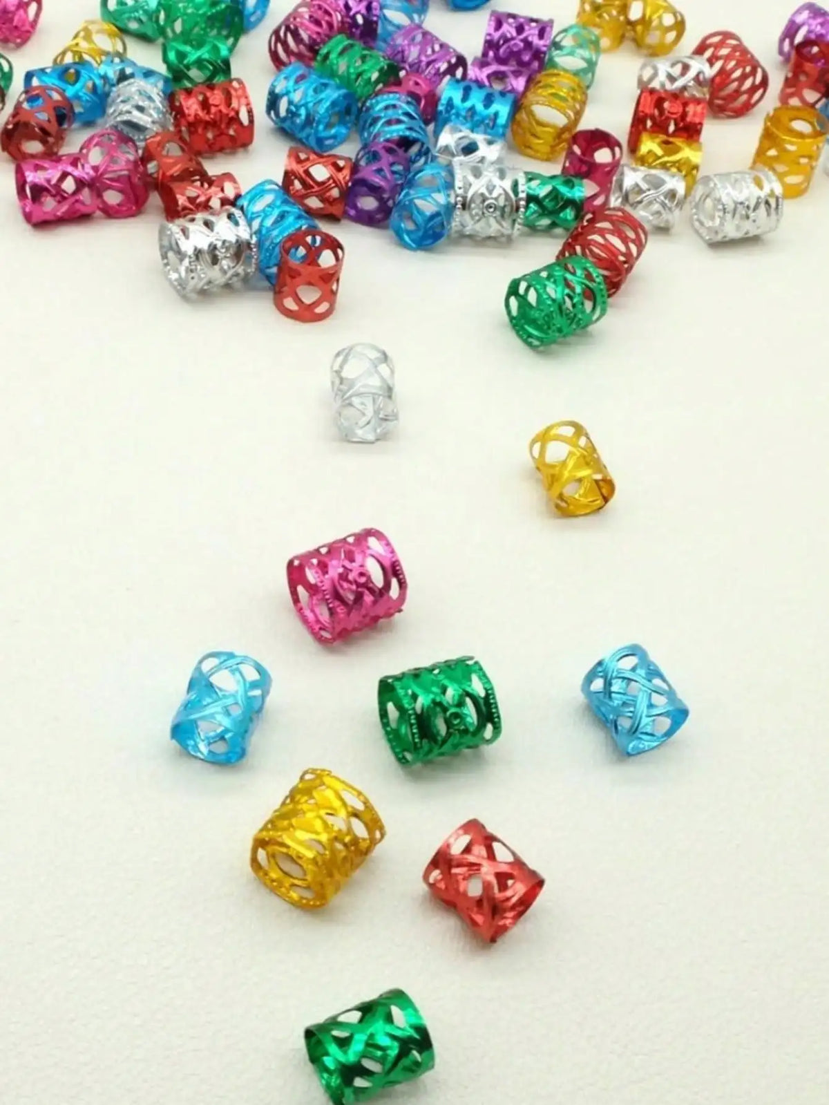 A collection of multicolor dreadlock hair rings in various metallic and plastic finishes scattered on a white background.