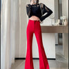 A woman models high-waist flare skinny red pants and a black top in a bright indoor setting.