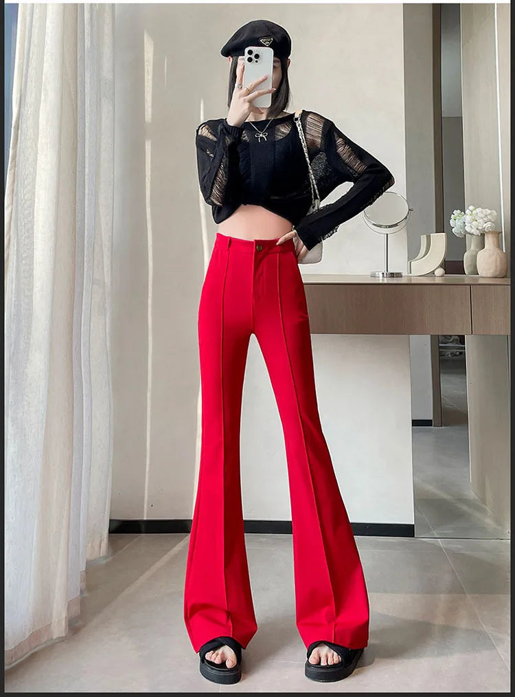 A woman models high-waist flare skinny red pants and a black top in a bright indoor setting.
