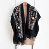 A black luxury floral scarf with intricate embroidery and fringe draped over a beige top.