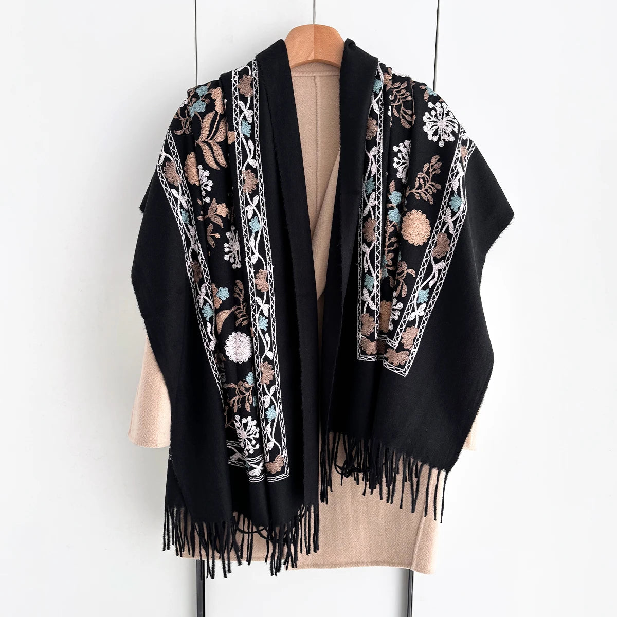 A black luxury floral scarf with intricate embroidery and fringe draped over a beige top.