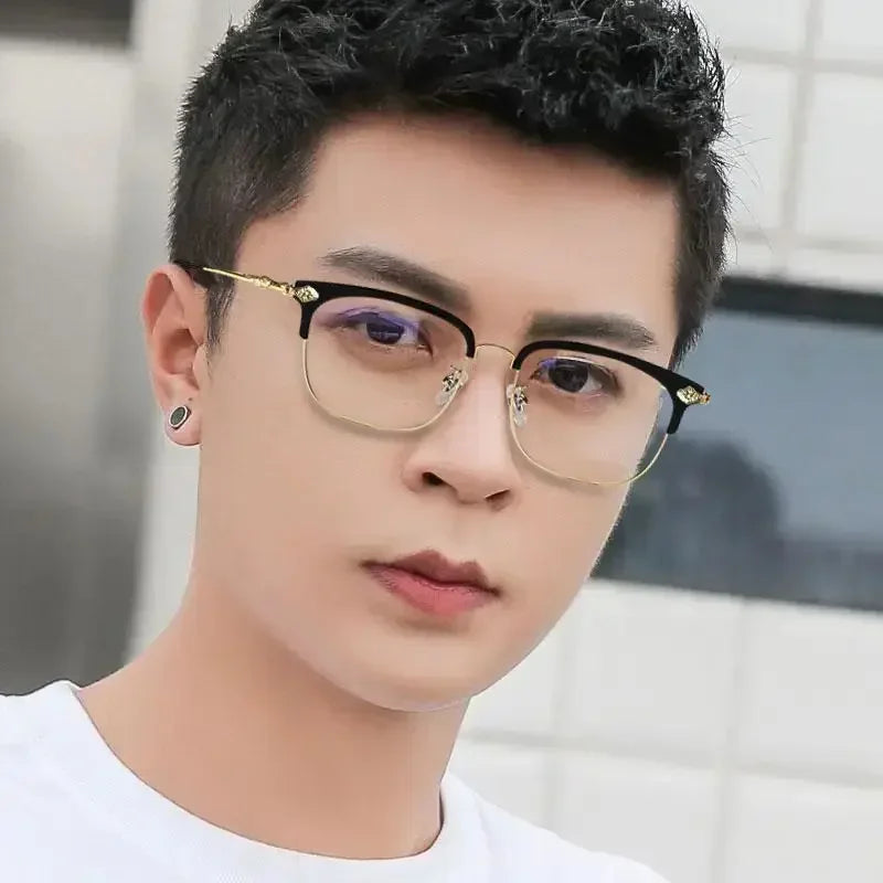 A close-up portrait of a young man wearing black half-frame reading glasses with gold accents.