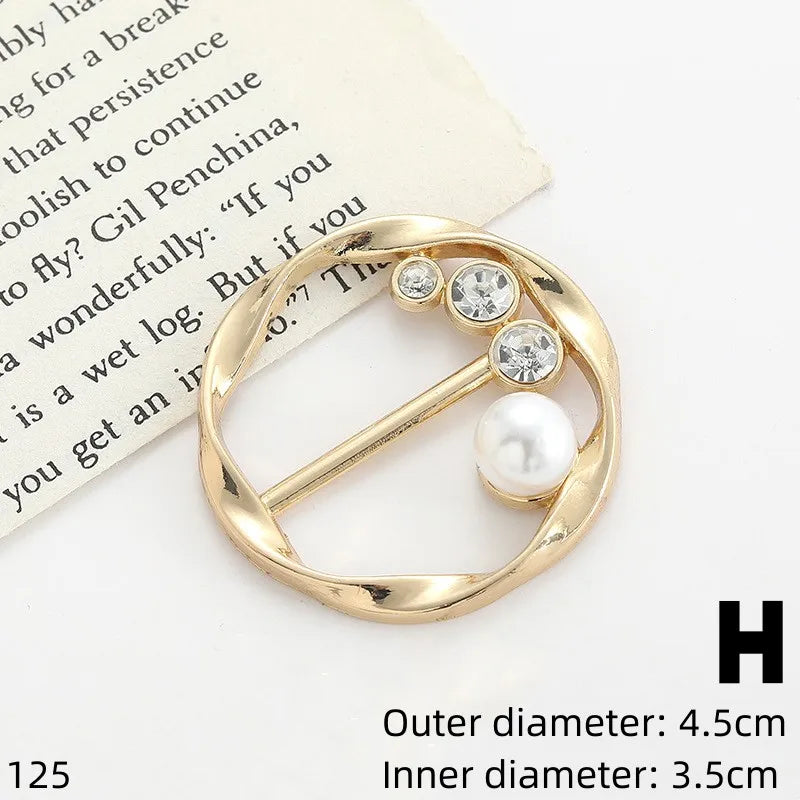 Gold-toned button clips featuring clear rhinestones and a white pearl, displayed on a textured paper background.