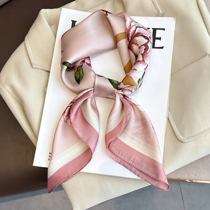 A pink and cream silk scarf tied in a bow, displayed on a white card against a beige fabric background.
