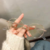 Une main tient une paire de lunettes à monture métallique transparente avec des accents dorés sur un fond clair.