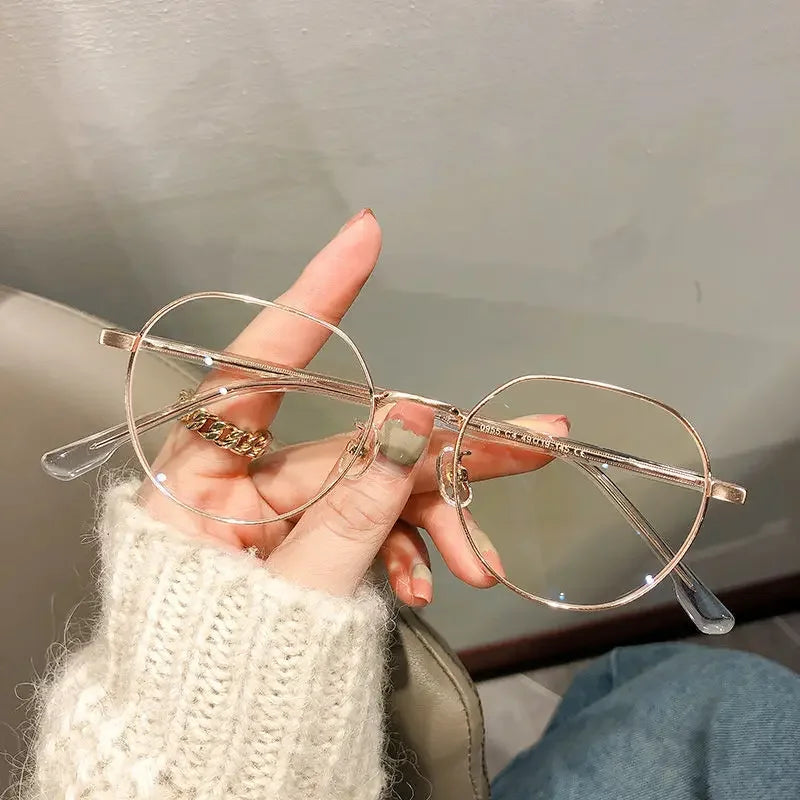 Une main tient une paire de lunettes à monture métallique transparente avec des accents dorés sur un fond clair.