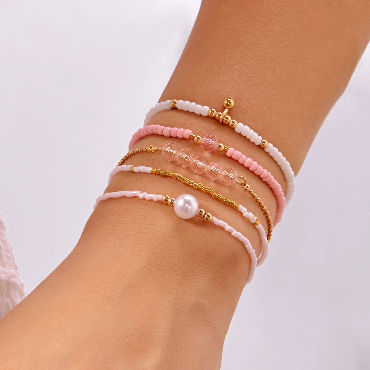 A stack of bohemian pearl beaded bracelets in shades of pink and white worn on a wrist.