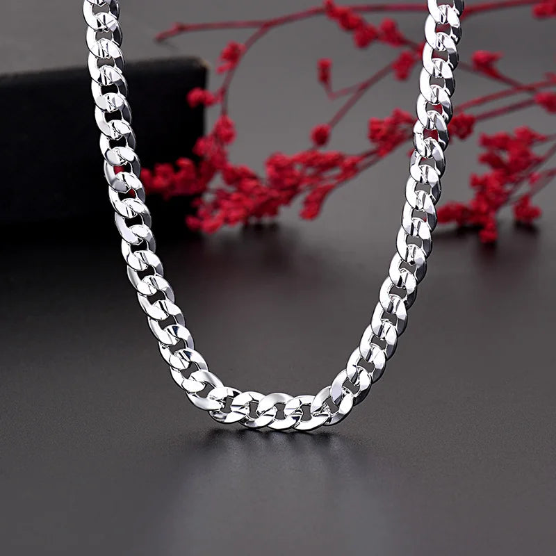 Un ensemble de pendentif et bracelet en argent, exposé sur un fond sombre avec des branches de fleurs rouges.