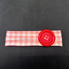 A pink and white checkered fabric headband with a large red button attached.