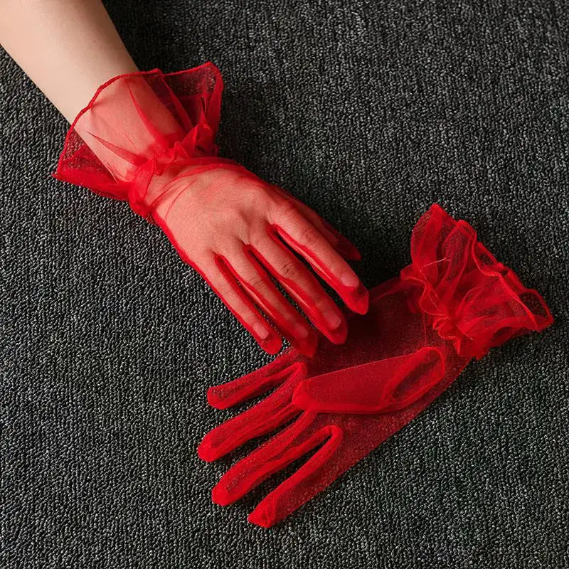 A hand wearing sheer red lace tulle finger gloves resting on a dark gray fabric.