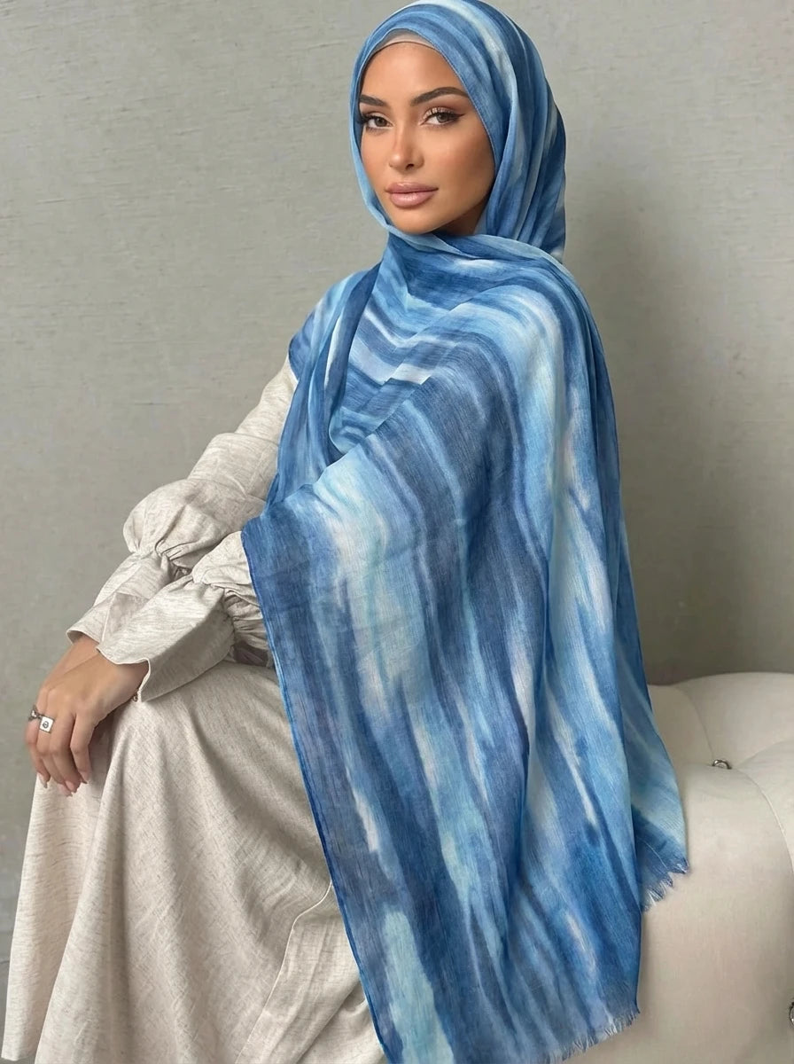 Una mujer vistiendo un pañuelo de hijab a rayas azules y blancas con una blusa beige clara.