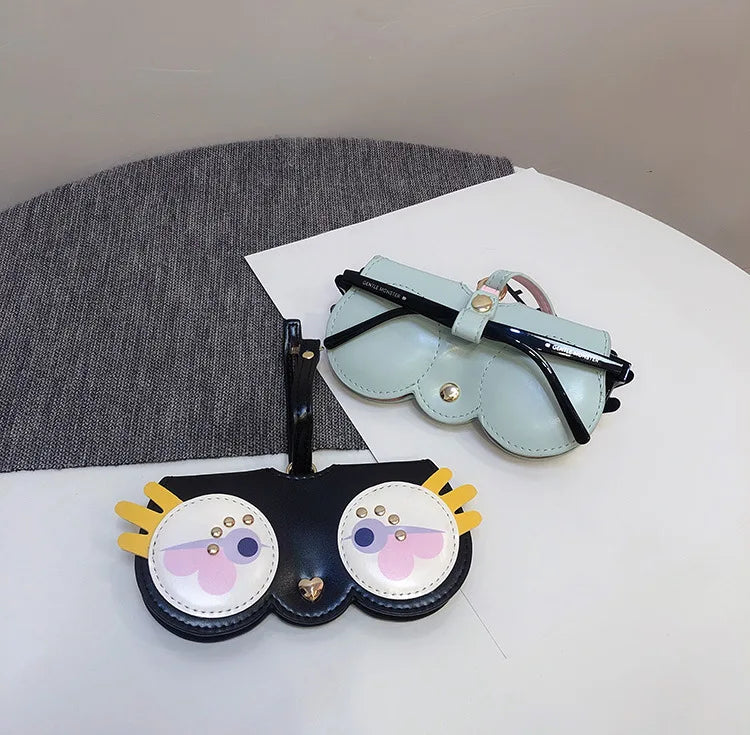 A light blue leather pouch with a black strap and two round, decorative patches is displayed on a white surface.
