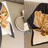 A black and gold floral print silk scarf draped on a beige surface.