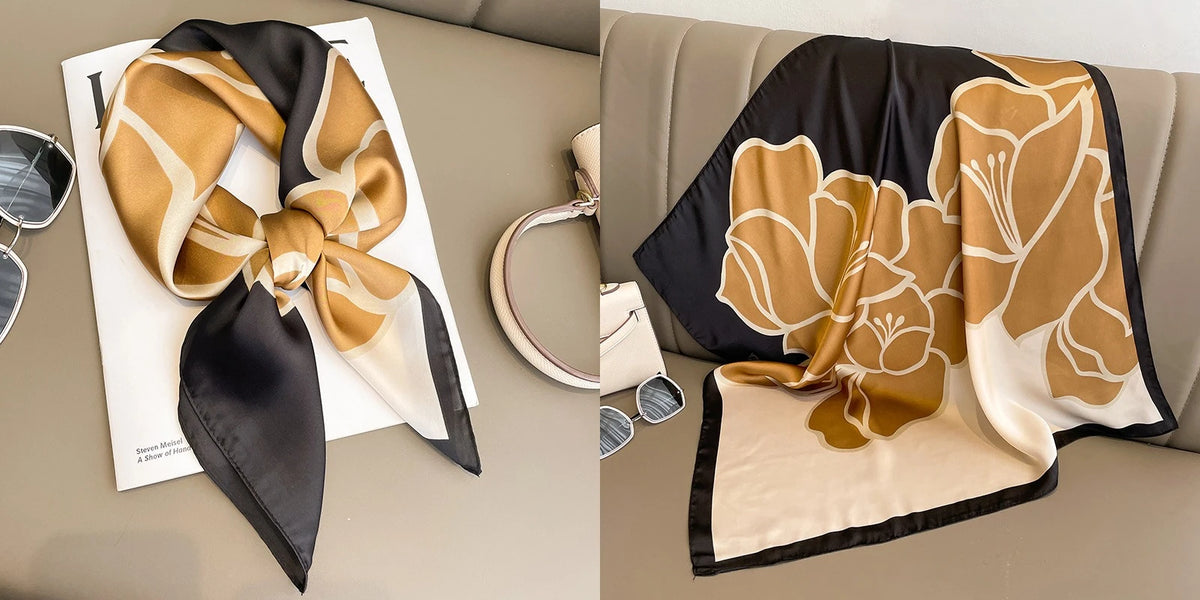 A black and gold floral print silk scarf draped on a beige surface.