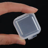 Eine Hand hält eine transparente Mini-Quadrat-Aufbewahrungsbox für Schmuck und Ohrringe vor einem dunklen Hintergrund.