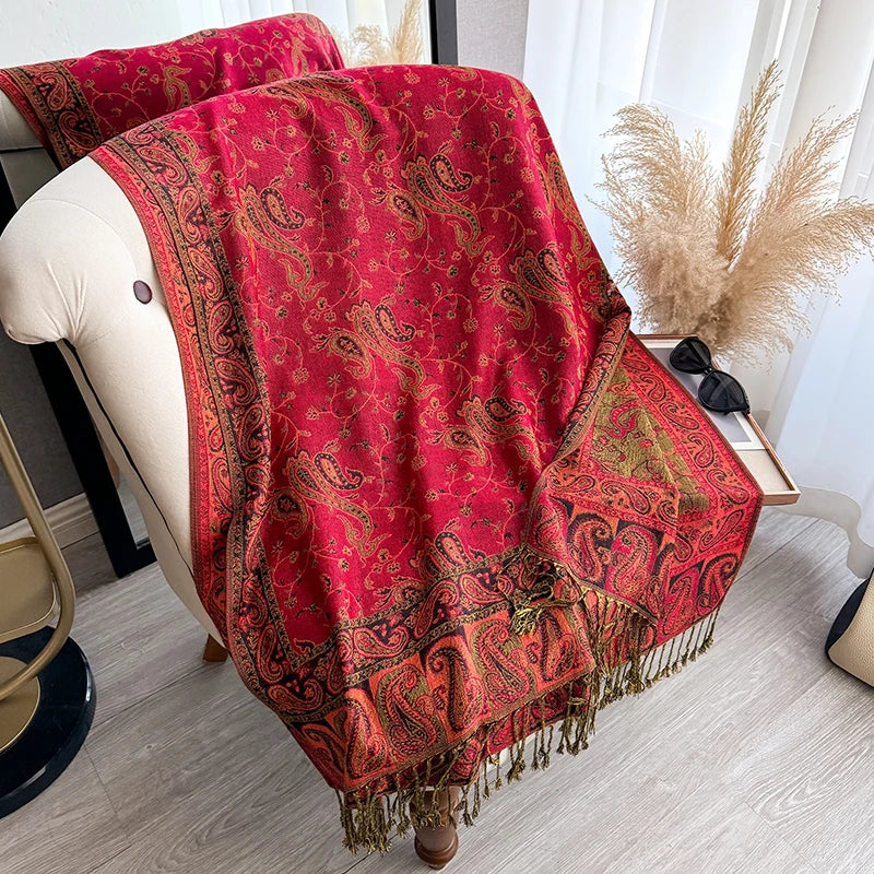 A vibrant red bohemian paisley tassel shawl draped over a white chair.
