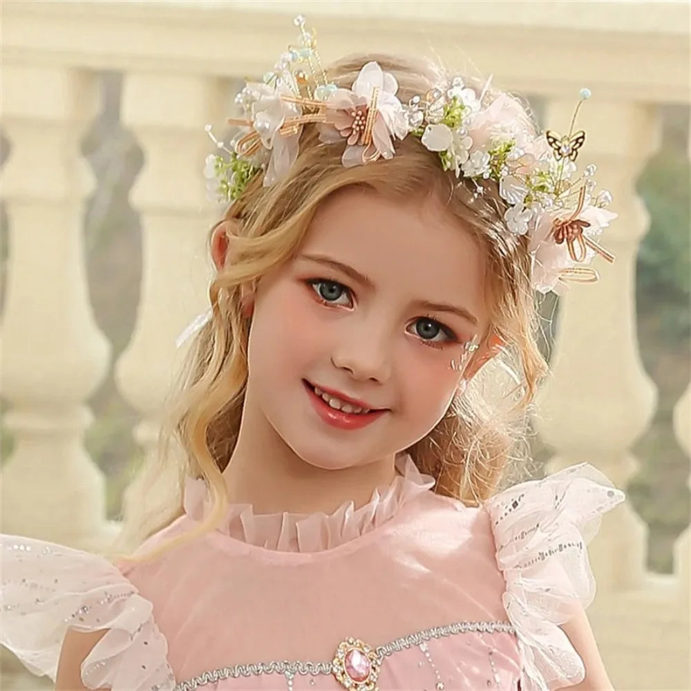 A young girl with blonde hair wears an elegant floral wreath headband and a pink dress.