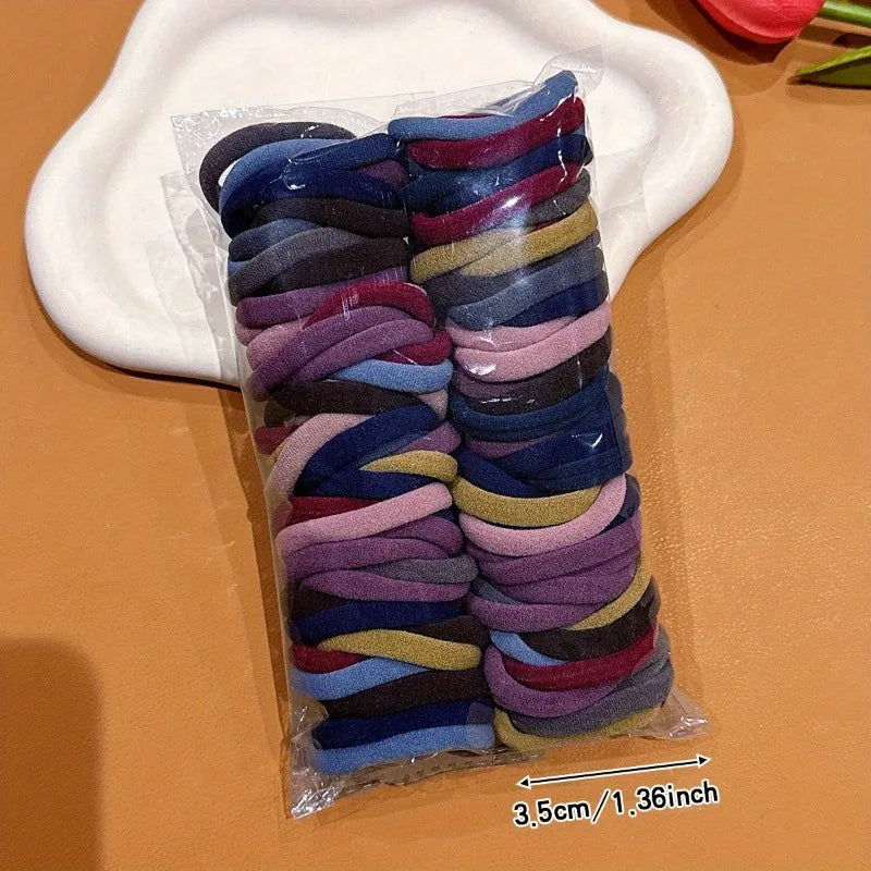 Ein Pack bunter elastischer Haargummis in verschiedenen Blautönen, Violett und Grau auf einer weißen Platte.
