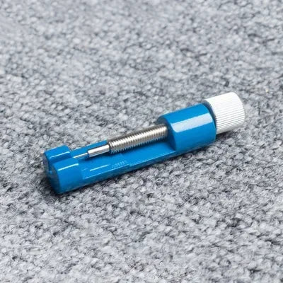A blue precision watch link pin remover tool with a silver threaded tip resting on a gray fabric surface.