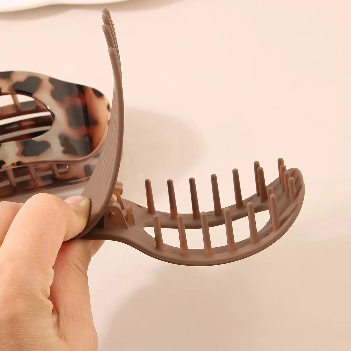 A hand is holding a brown matte oval hair claw clip with a leopard print design.