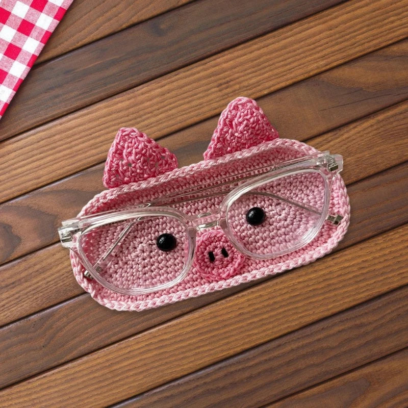 A handmade crochet pink pig face eyeglass storage case resting on a wooden surface.