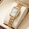 Reloj de pulsera analógico de cuarzo en tono dorado con caja cuadrada y pulsera, exhibido en una caja de color claro.