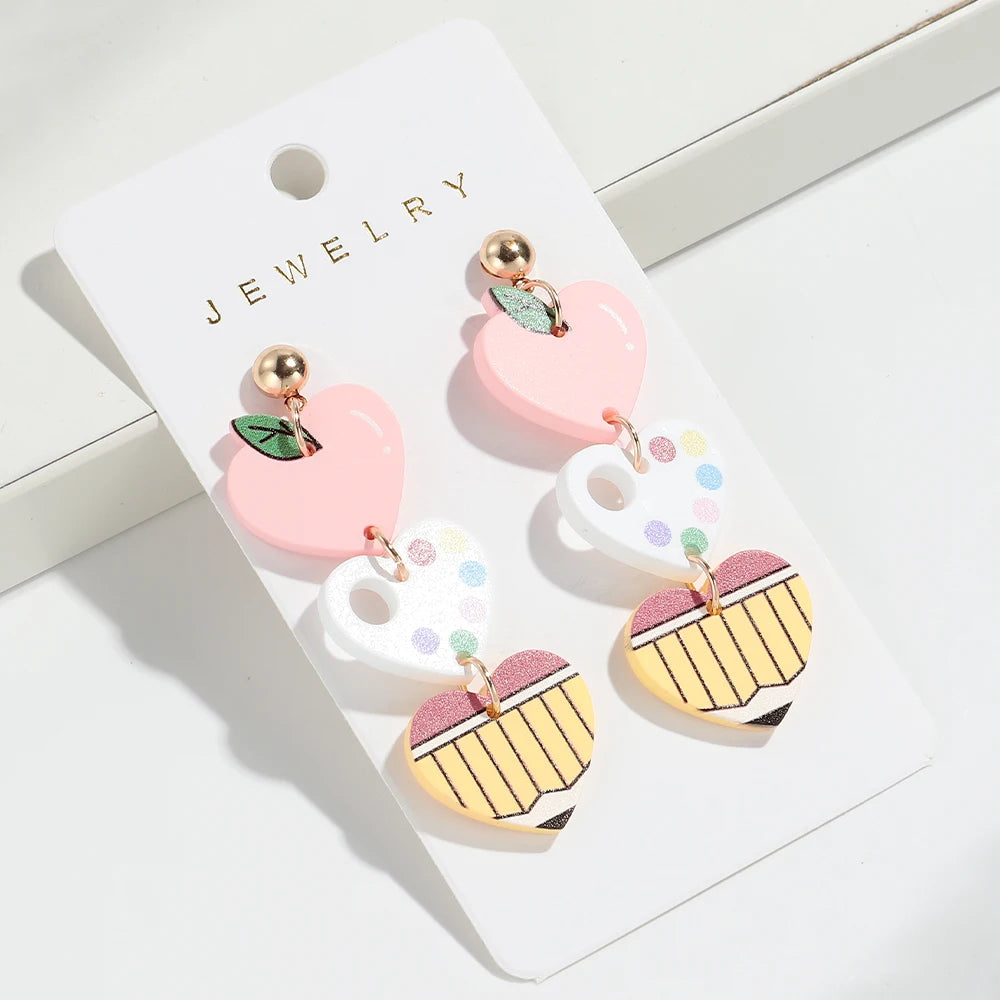 Un par de pendientes en forma de corazón rosa y blanco con detalles dorados, mostrados en una tarjeta blanca.