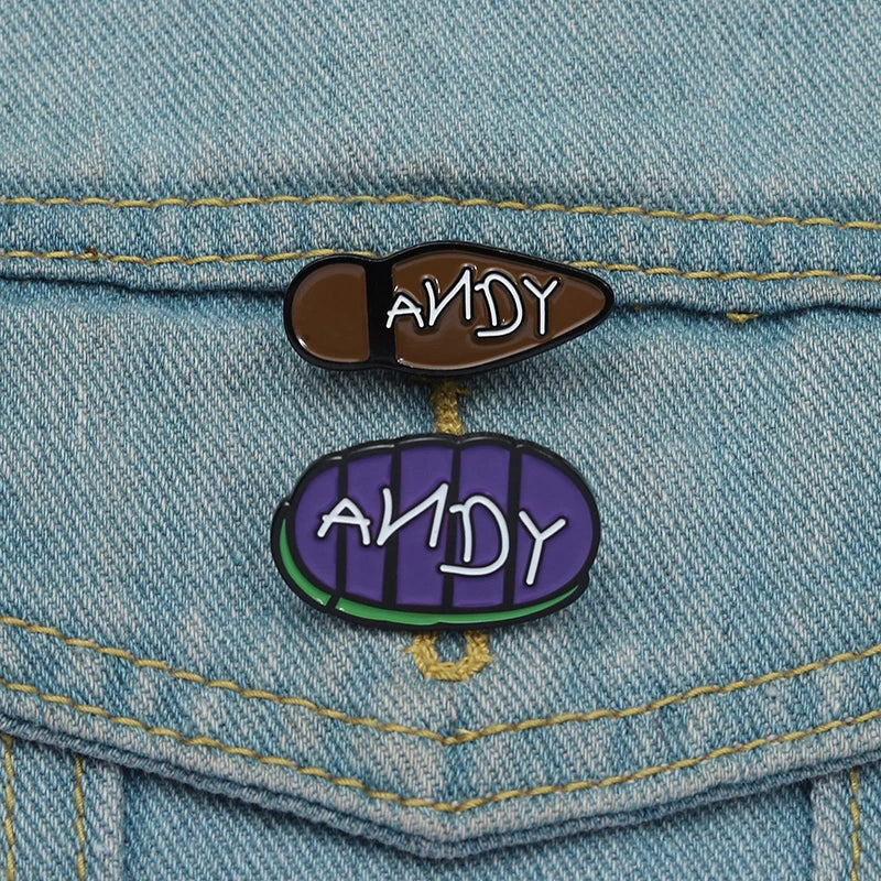 دبوسان تطريز من الإنميل على شكل يحمل اسم ANDY بخلفية قماش جينز.