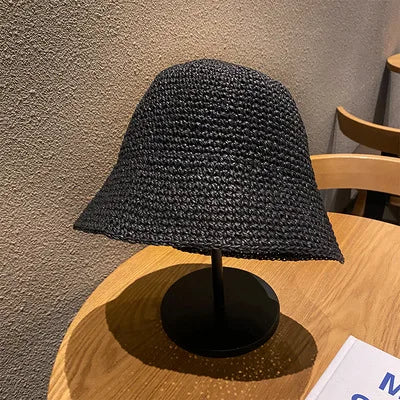 A black hand-woven straw visor hat displayed on a wooden surface against a gray wall.