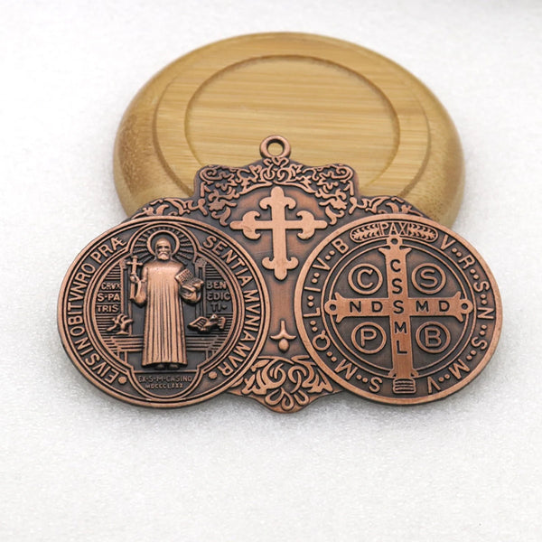 Médaille de bronze ronde représentant Saint Benoît et symboles religieux, sur fond clair.