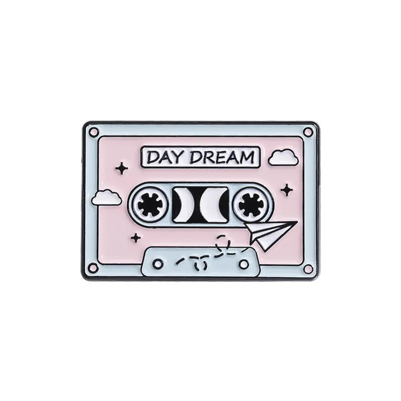 A pink enamel pin featuring the text DAY DREAM and a stylized cassette tape design.