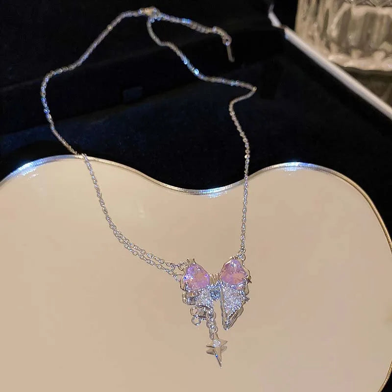A delicate silver necklace featuring a pink heart zircon charm and a star pendant displayed on a dark velvet background.