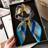 A blue and gold silk scarf tied in a bow displayed in a black box.