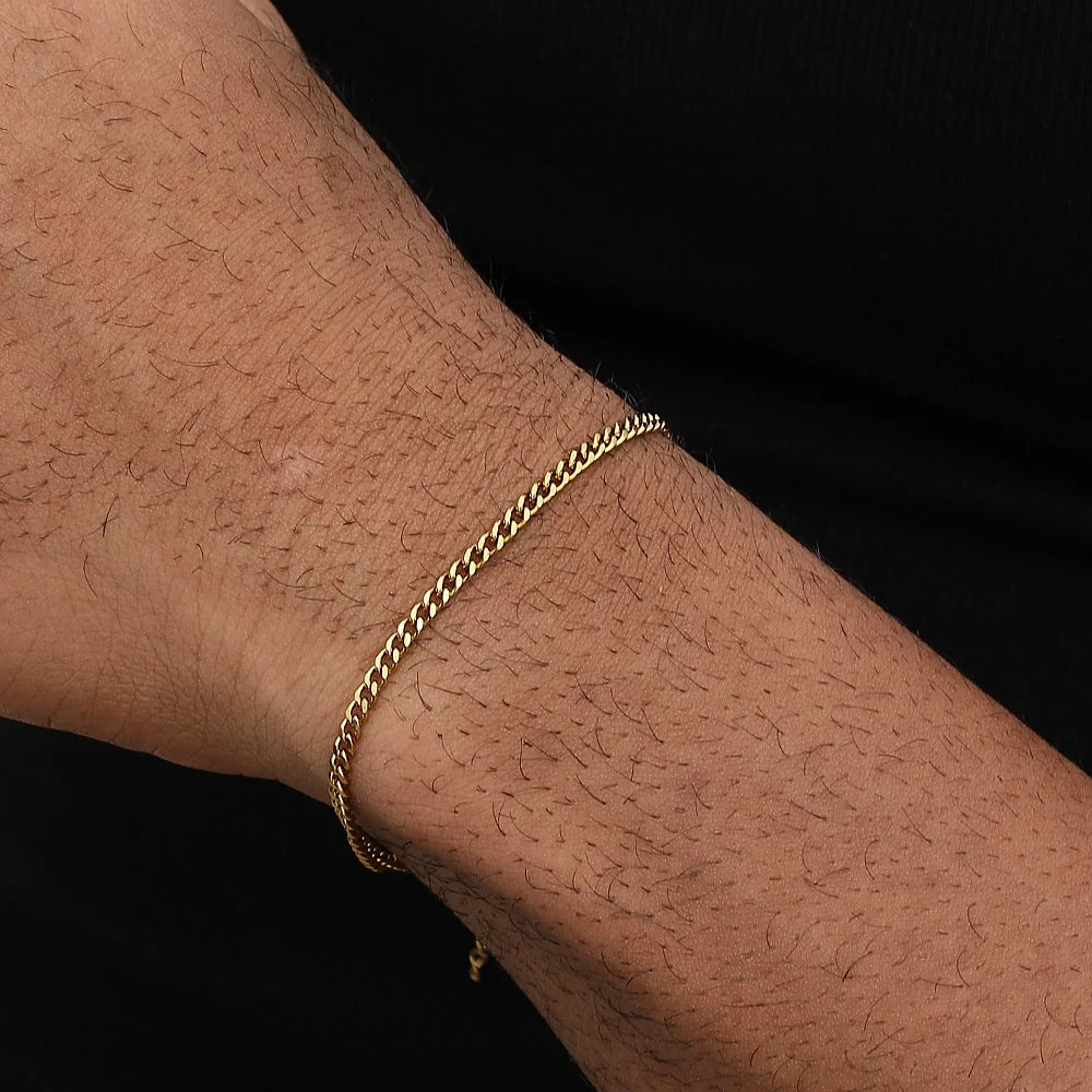 A close-up of a man's wrist wearing a gold-toned stainless steel Cuban link bracelet.
