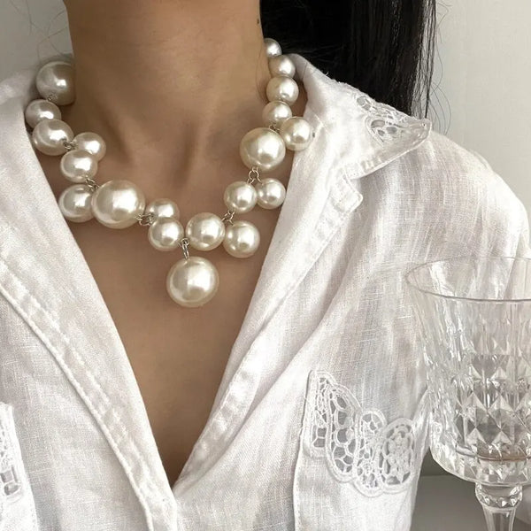 A close-up of an elegant simulated pearl choker necklace worn against a white shirt.