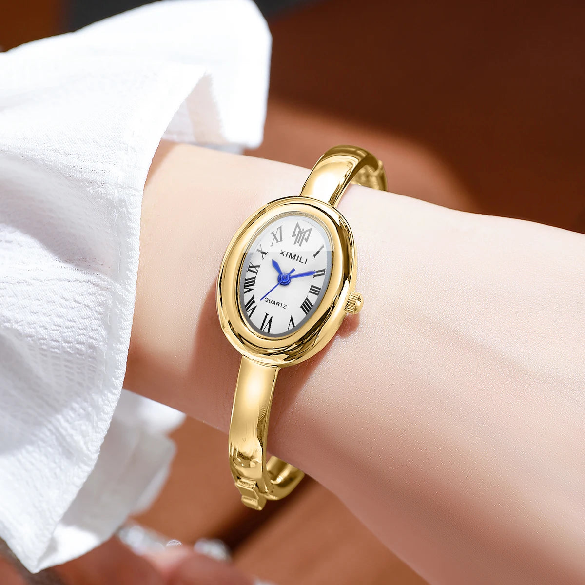 A close-up of a gold-toned quartz watch bracelet with a white face and blue hands worn on a wrist.
